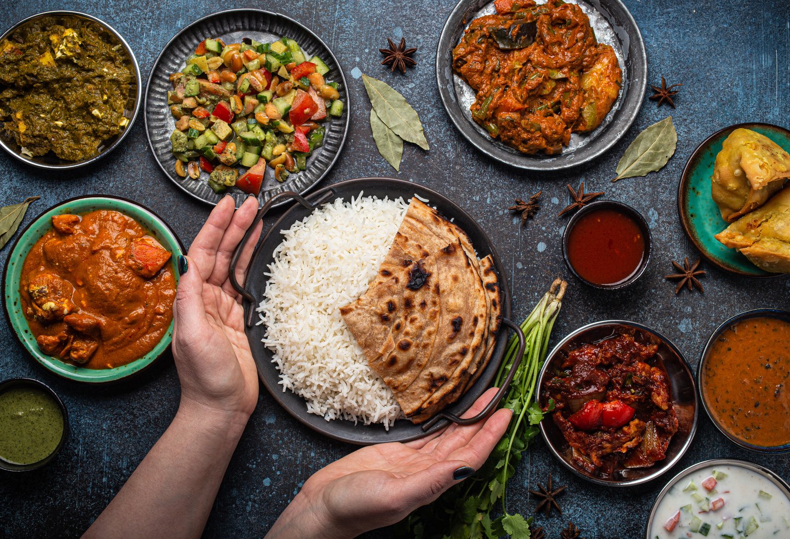 Female Hands Serving Indian Ethnic Food Buffet on Rustic Concret